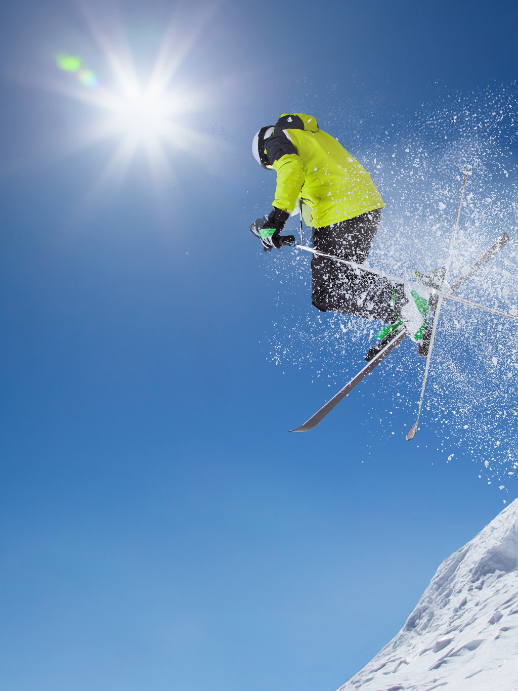 A skier dressed in black and fluorescent green performs a jump in the snow