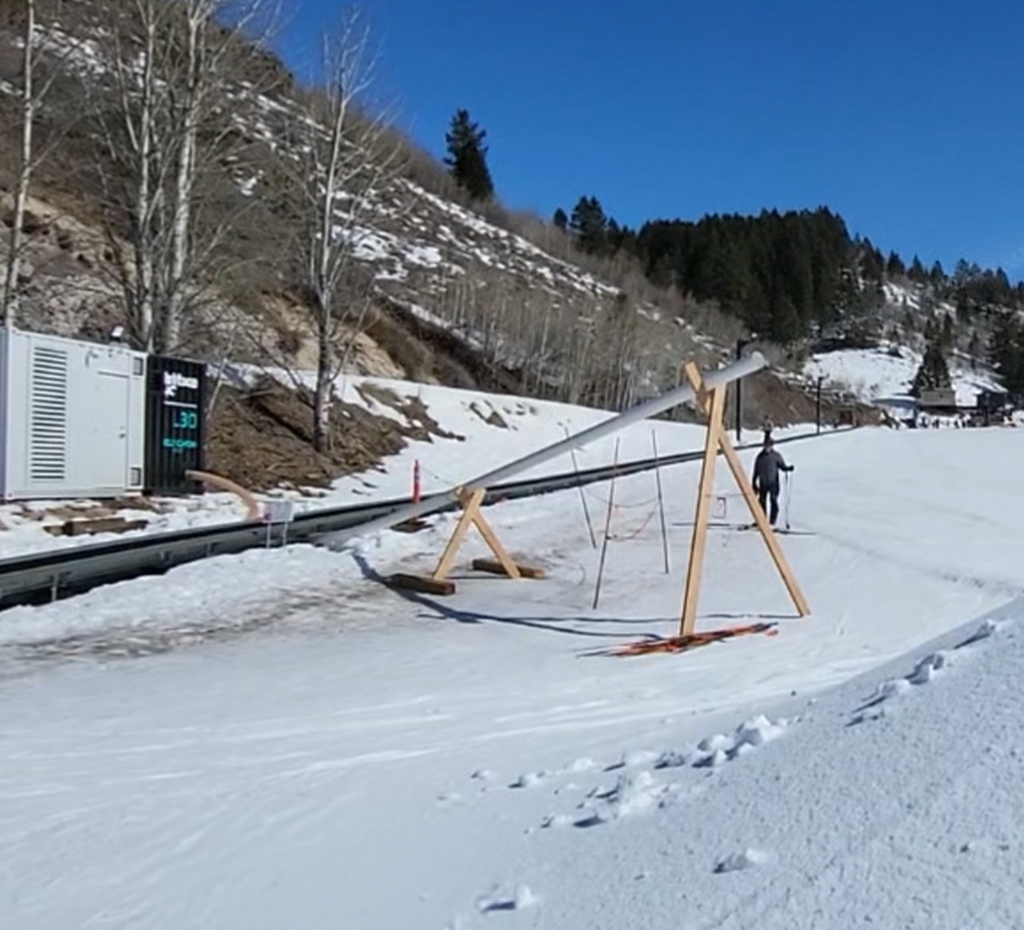 Gens qui ski pendant que la machine L30 de Latitude90 propulse de la neige sur la montagne - People skiing while the Latitude90 L30 machine blasts snow onto the mountain