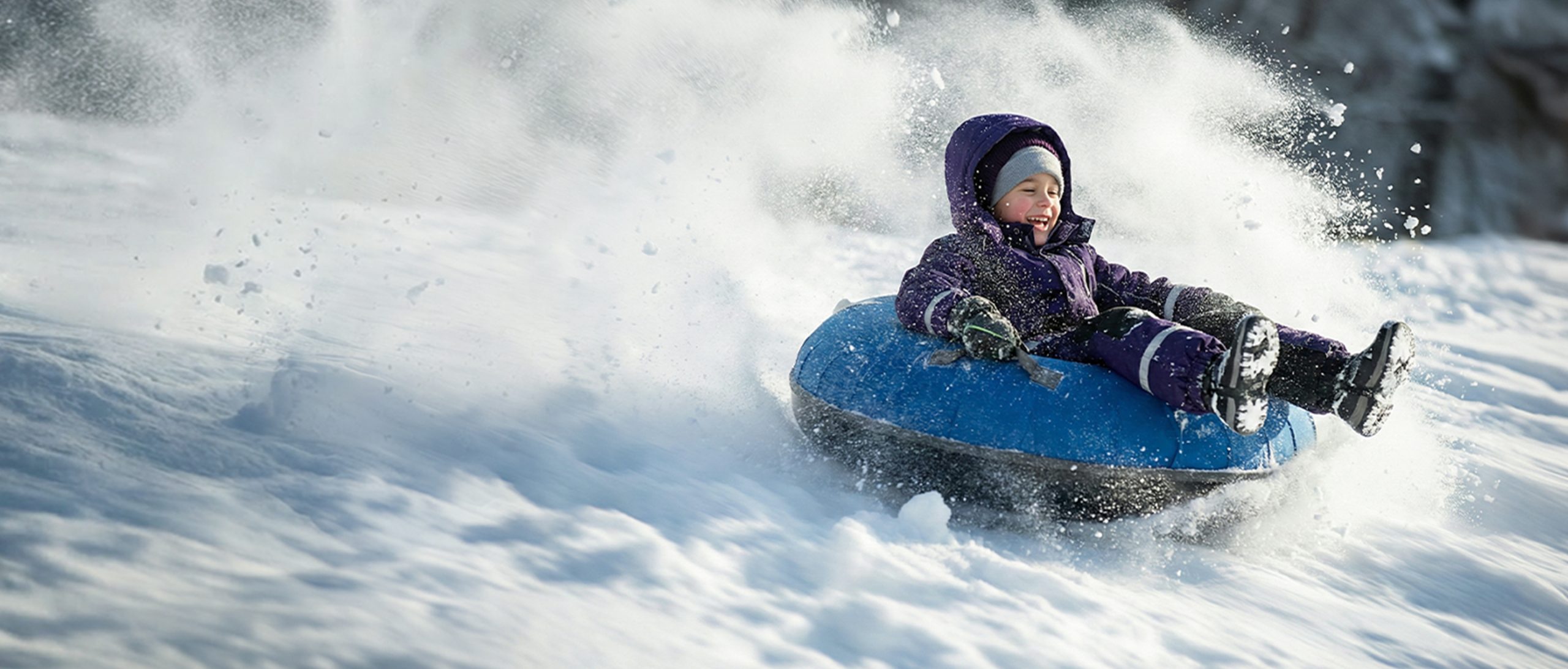 A young boy in a snowsuit, having great fun sliding down a snowy slope on a tube