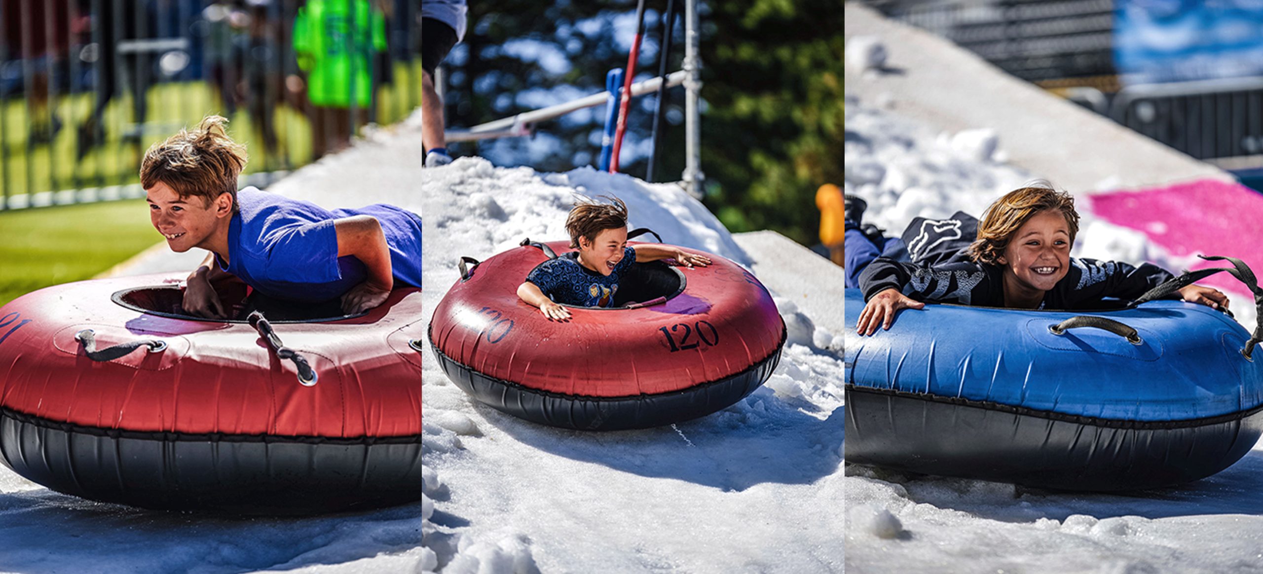 Three young boys dressed in summer clothes, seated on tubes, are sliding down snowy slopes.
